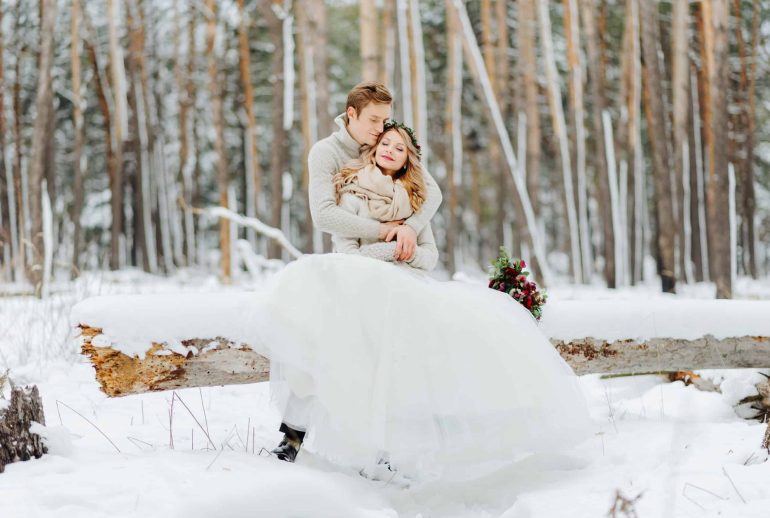 Couple in love are hugging on background of the snowy forest. Winter wedding.